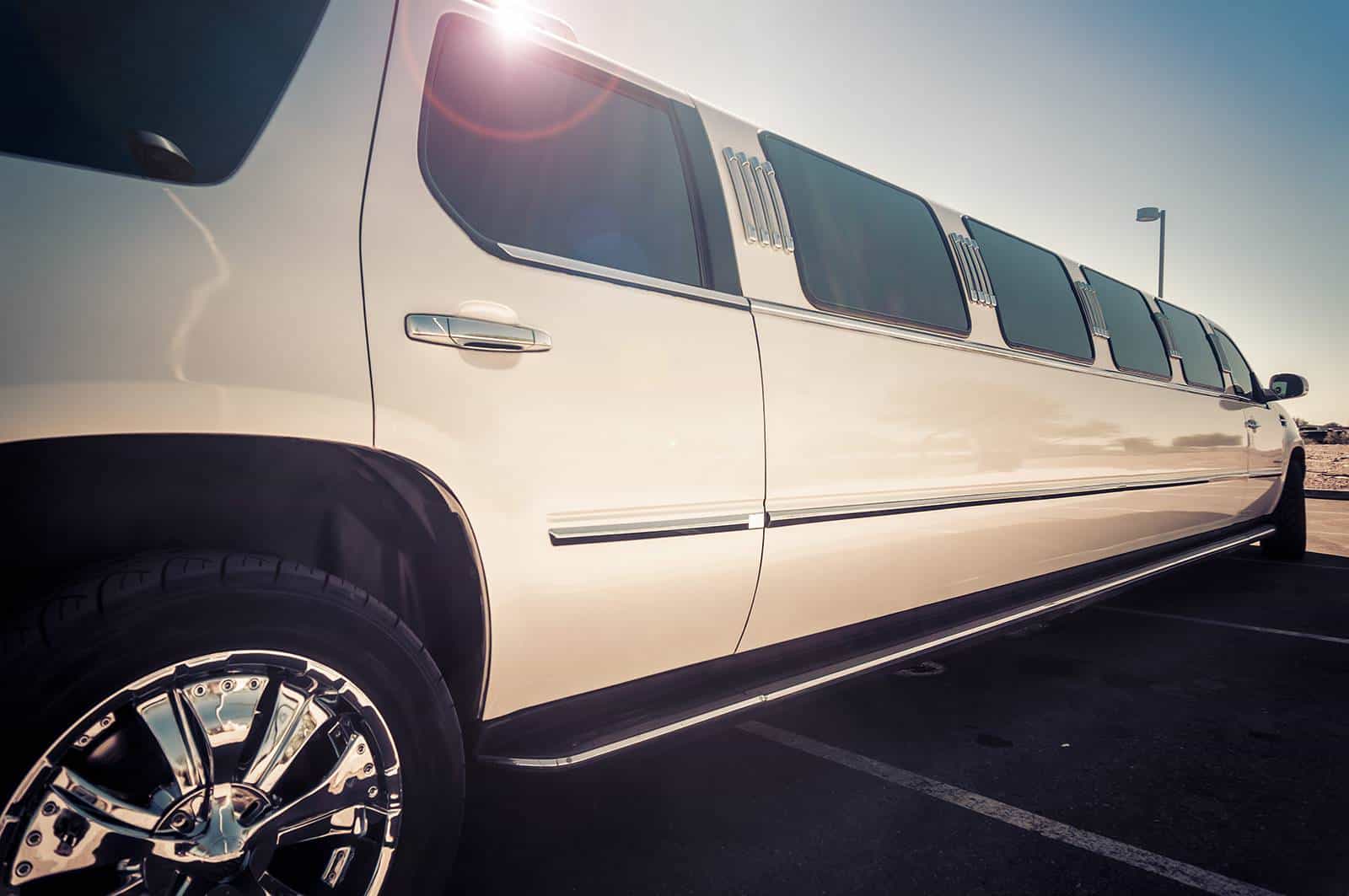 Elegant white limousine parked outdoors with sunlight glare.