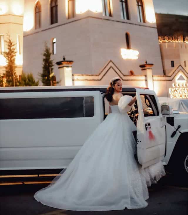 Bride in wedding dress getting into limousine outside church.