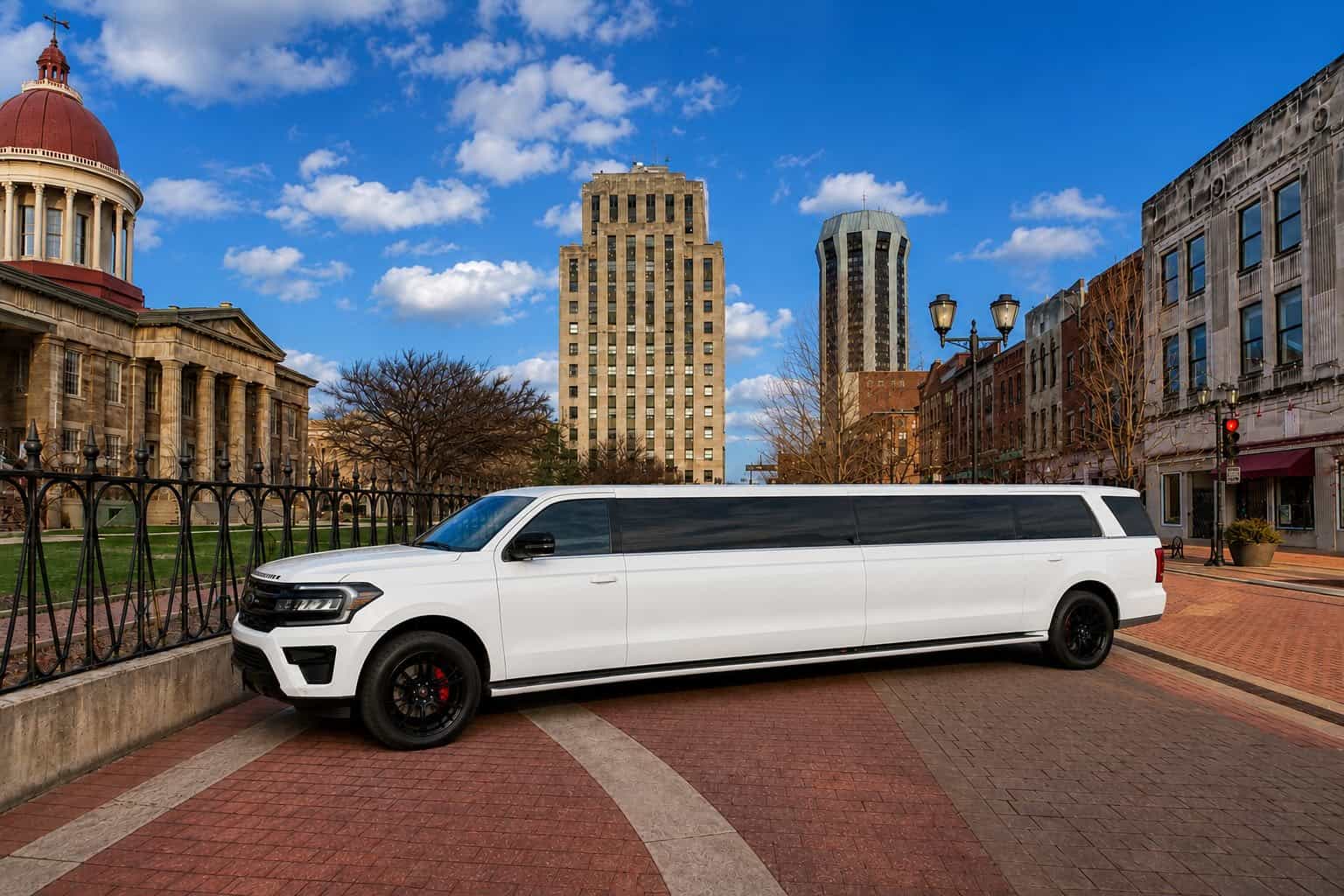 White limousine parked on city street with historic buildings and blue sky.